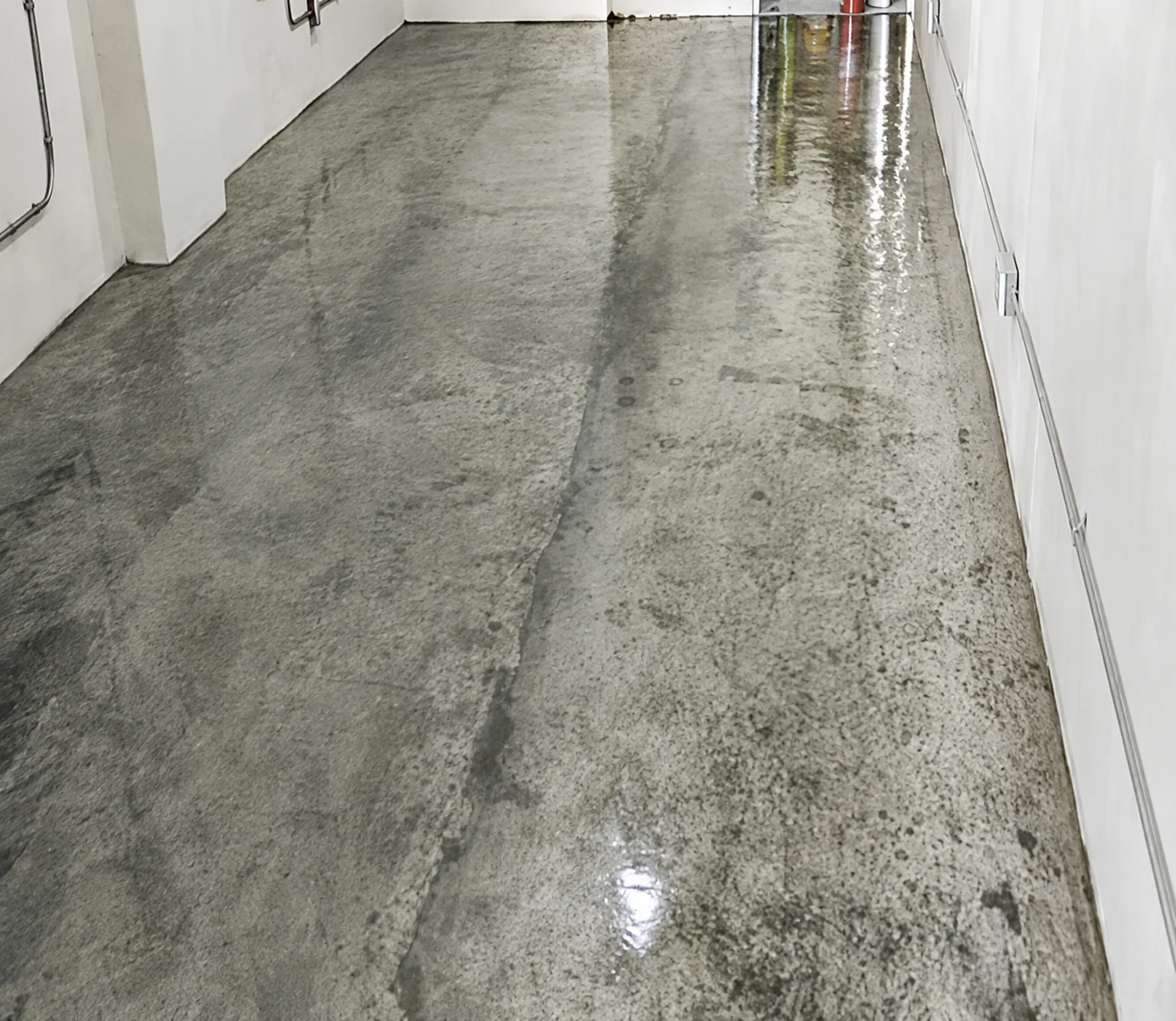 Bare, patchy concrete floor in a narrow corridor before ESD coating, showing stains, old adhesive marks and an uneven surface.