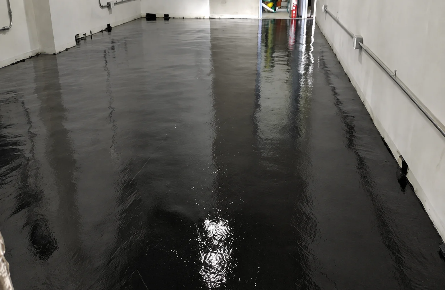 Freshly applied black conductive base coat covering the floor wall to wall, still wet and reflecting the room lights.