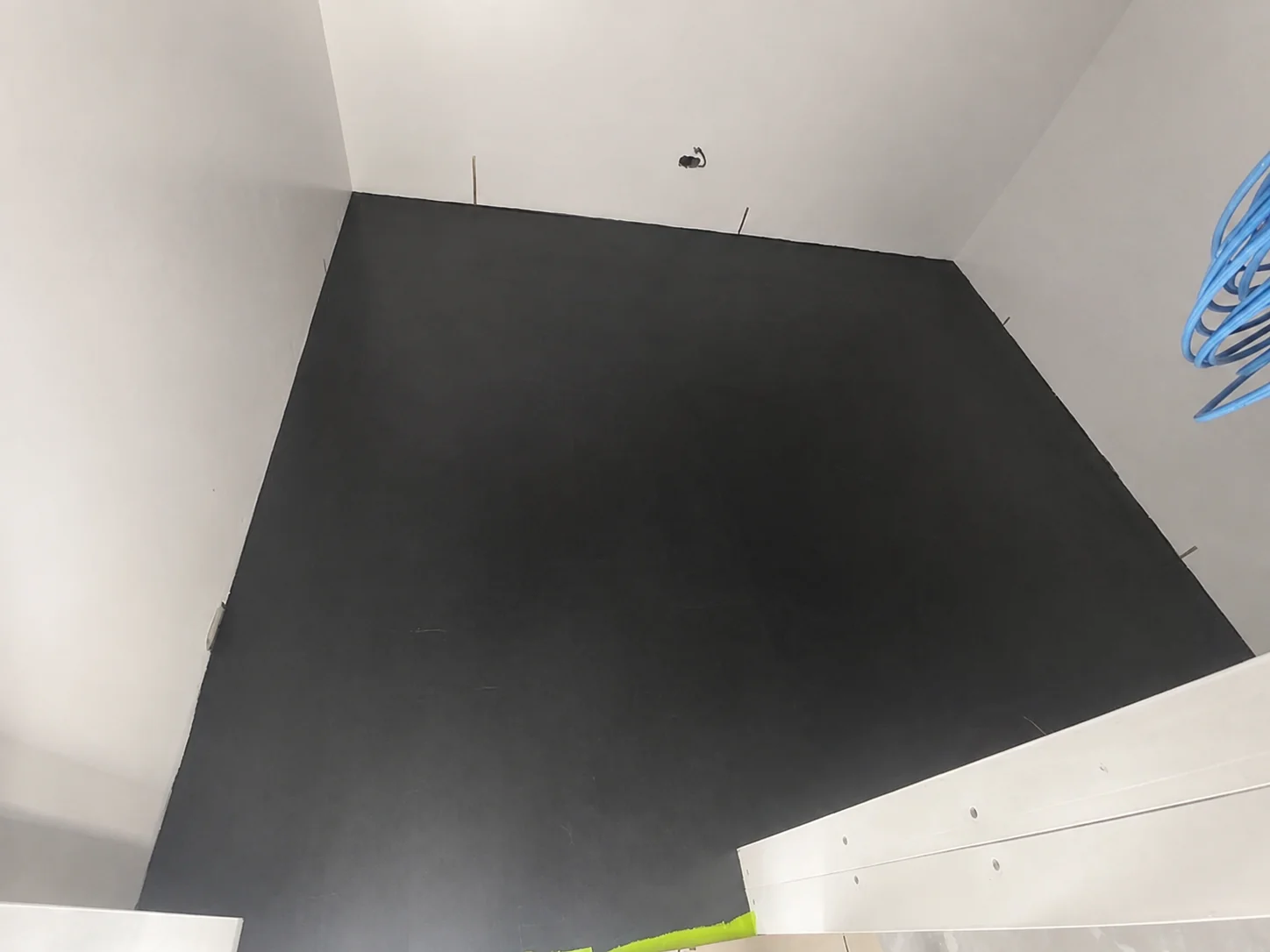 A room-sized black conductive base coat, fully applied and curing, with copper tape tails left exposed at the wall edges.