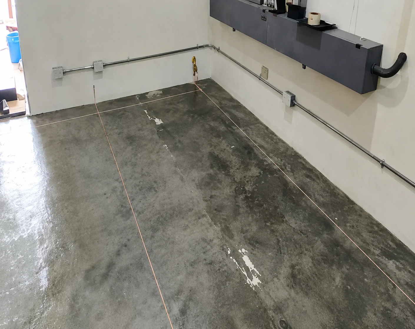 Copper grounding tape laid in long parallel runs across a prepared concrete floor, with a grounding connection point at the wall and conduit running above.