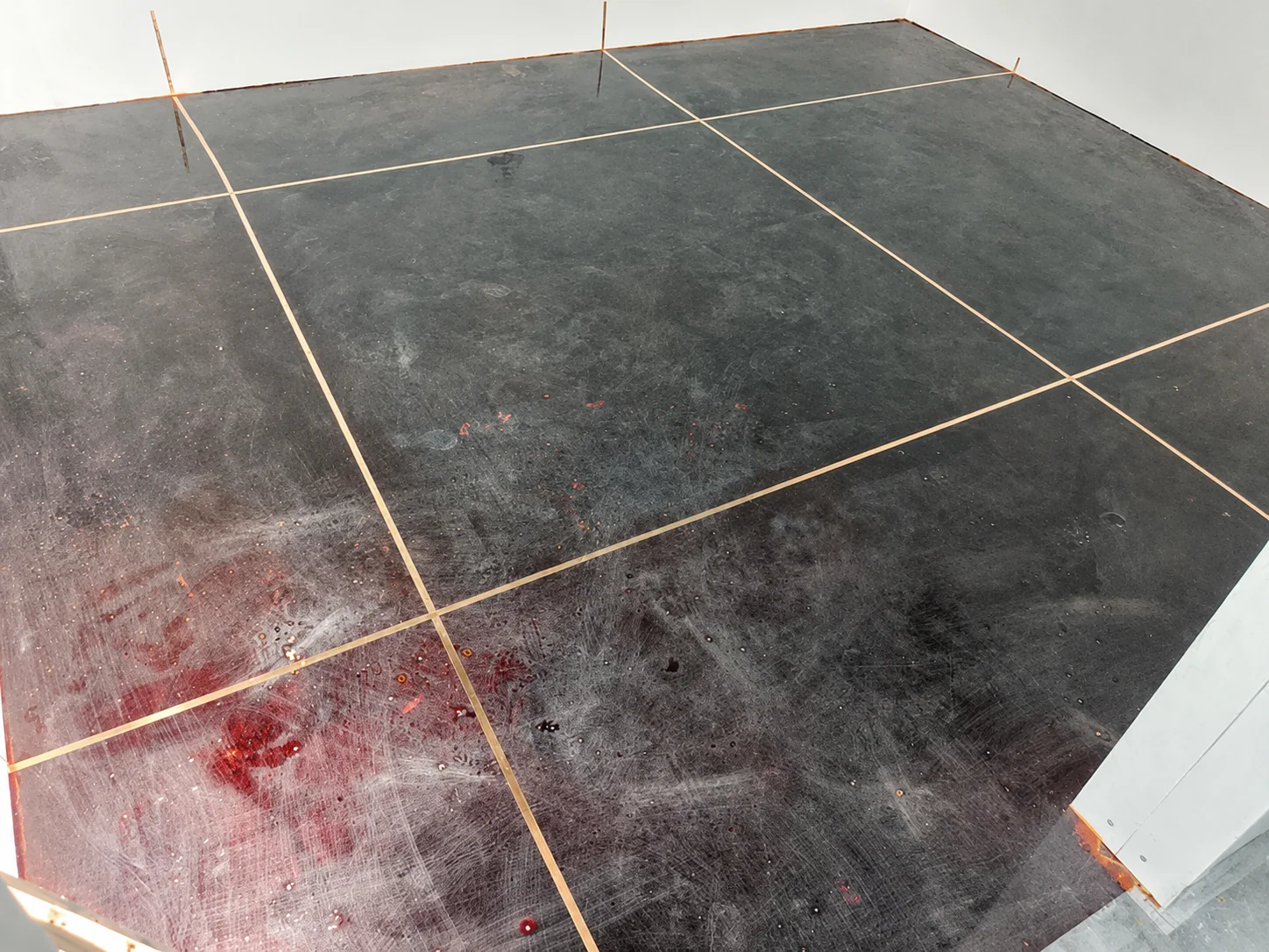 Copper grounding tape laid in a grid across a dark primed floor, with tape tails turned up at the wall ready for connection.