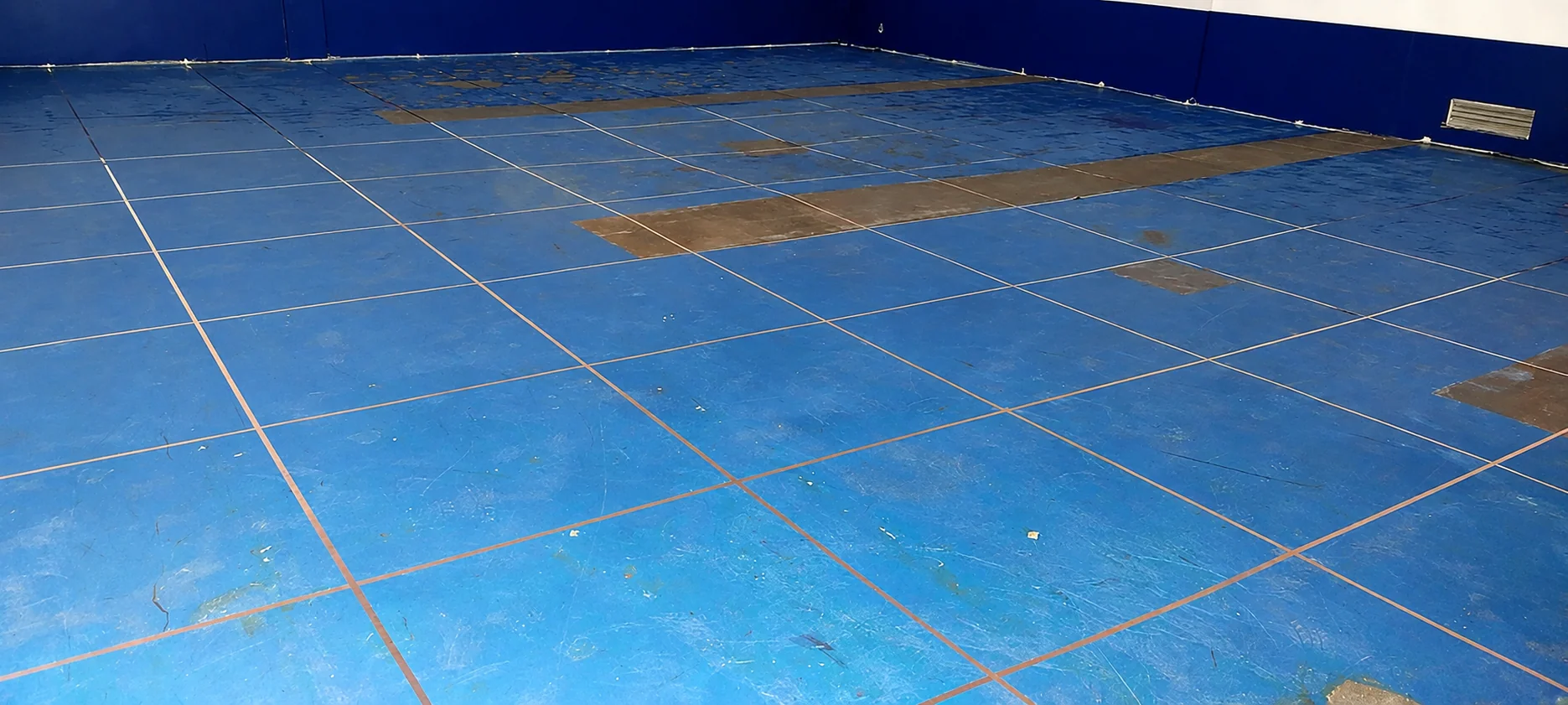 Close view of the existing blue ESD tile floor showing the copper grounding grid running along the tile joints, with worn and patched areas.