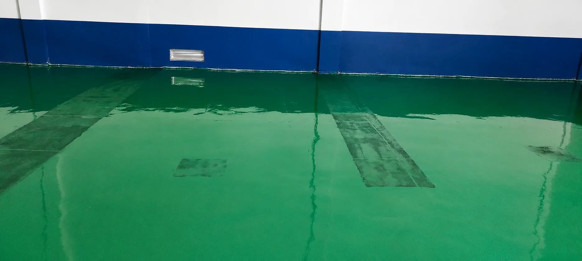 Close view of the finished green ESD epoxy floor meeting the blue wall skirting, with a coved edge and a floor vent above.