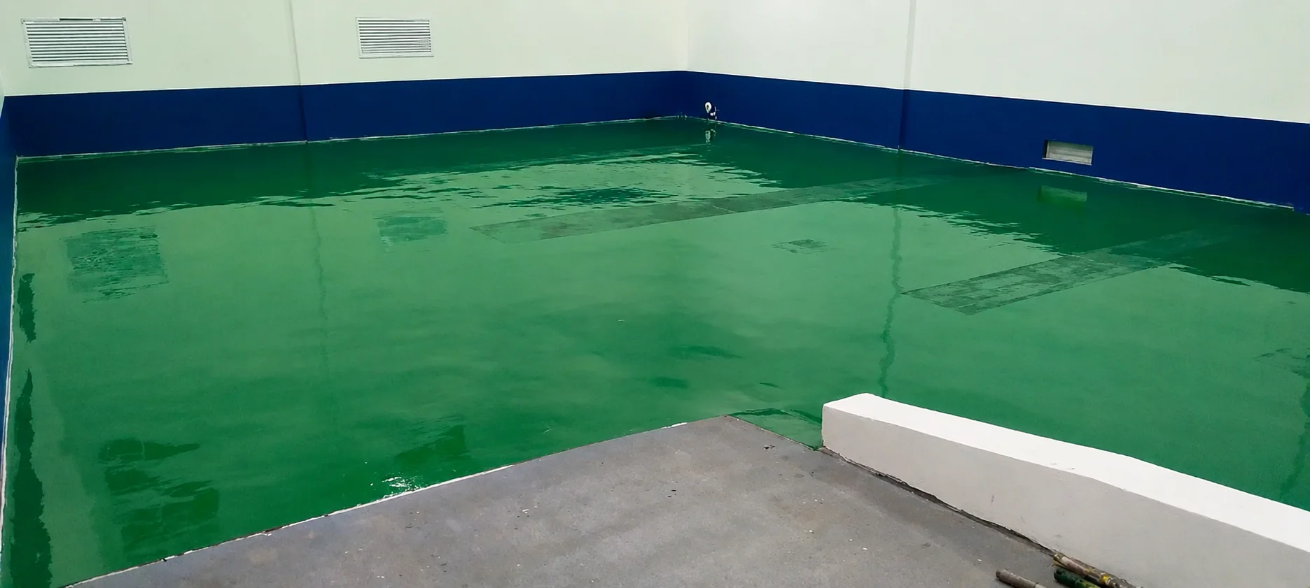Wide view of a completed green ESD epoxy floor with a mirror-like finish, bounded by blue skirting and a concrete threshold.