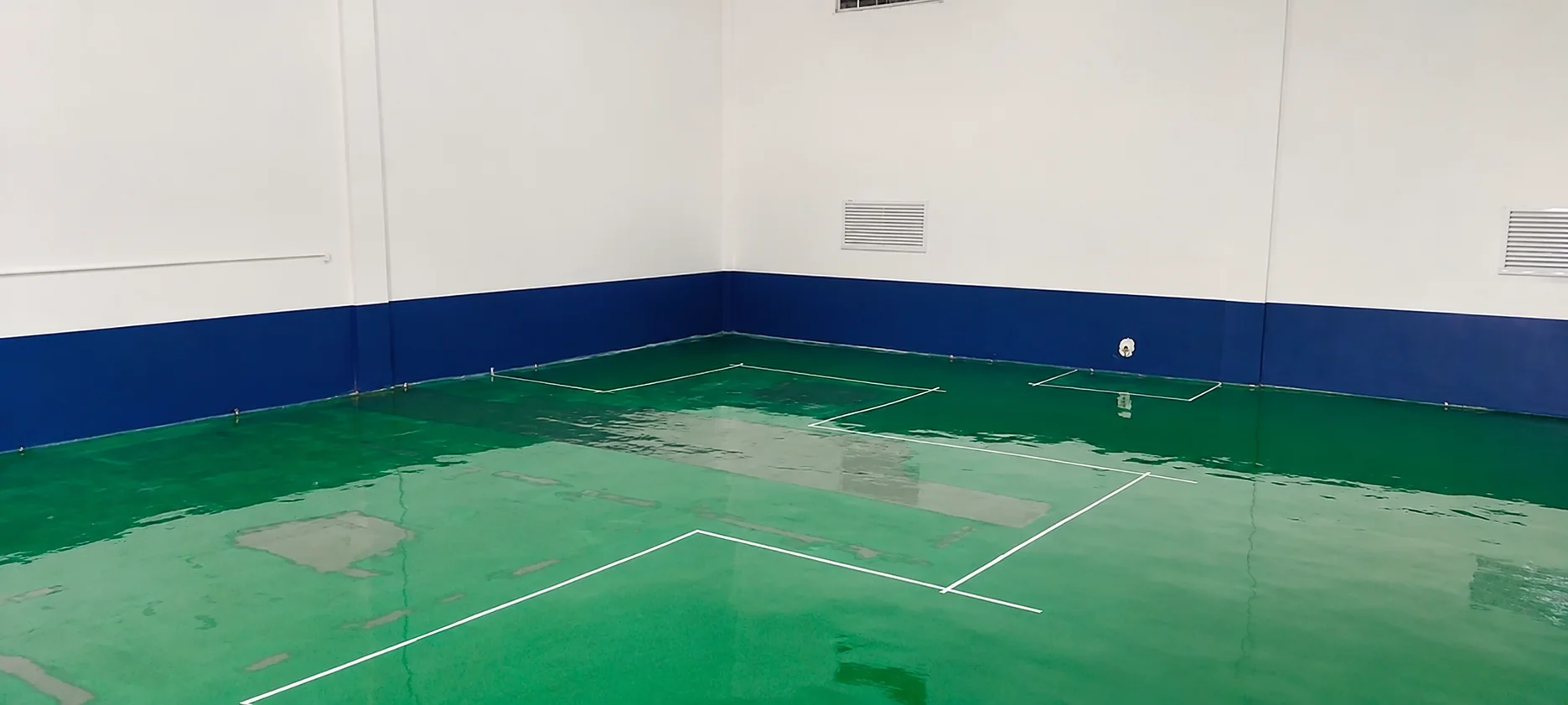 Finished glossy green ESD epoxy floor with white grid lines and copper grounding strips, meeting a blue and white wall.