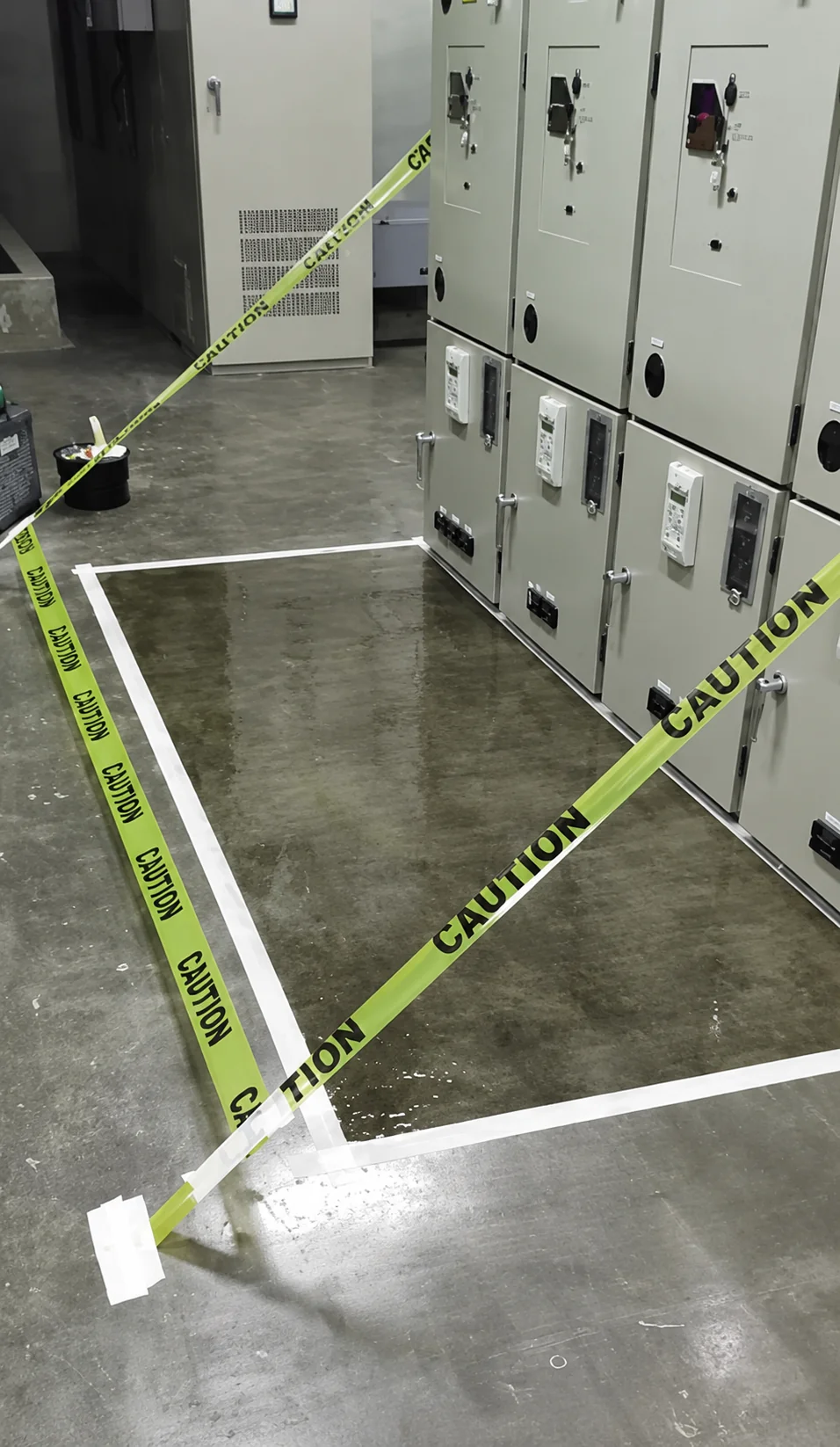 Work area in front of an electrical switchgear lineup, masked out with white tape and cordoned off with yellow caution tape before ESD coating.