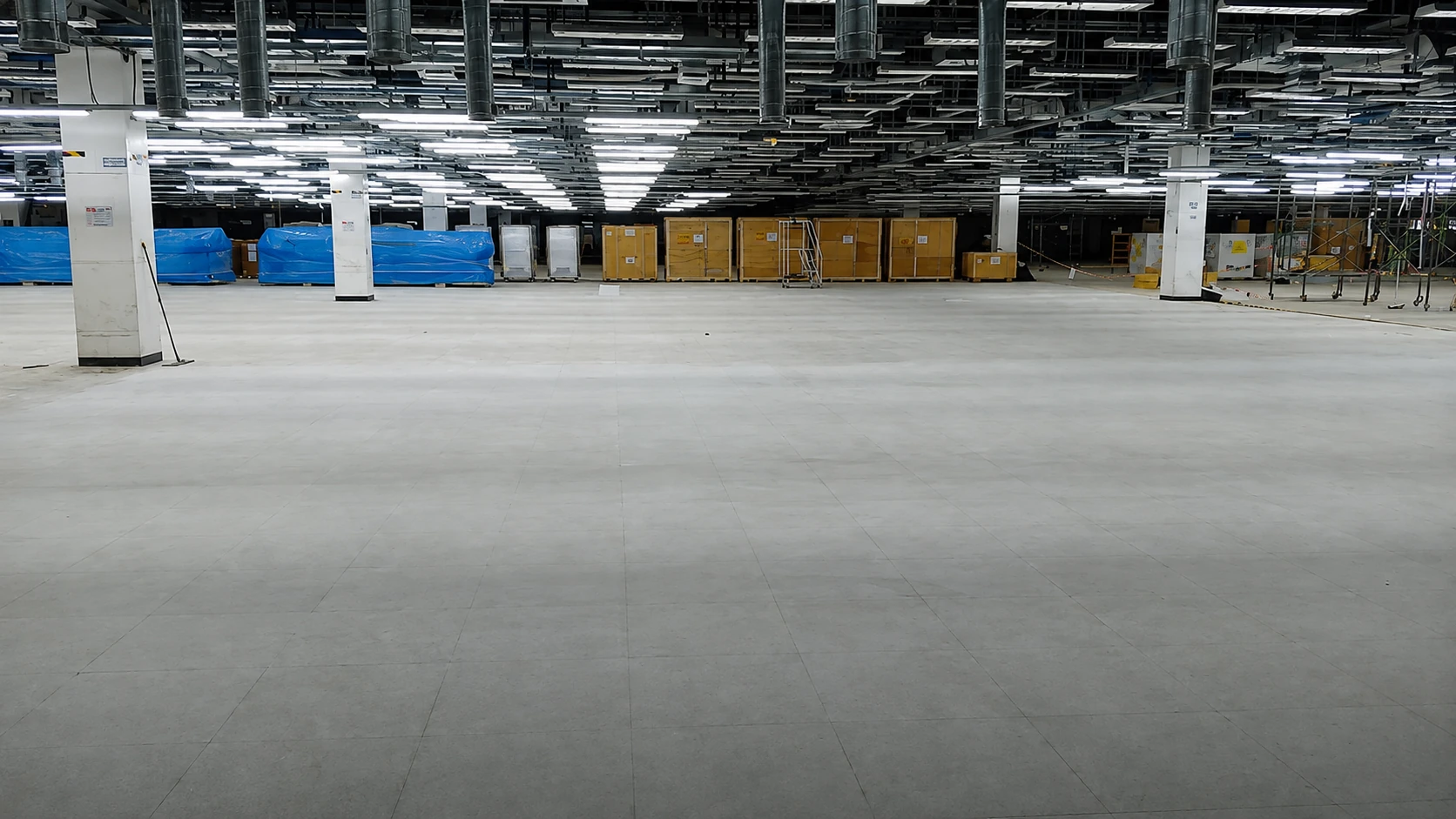 Smoothed subfloor in a production facility with crated equipment staged along the wall before ESD floor installation